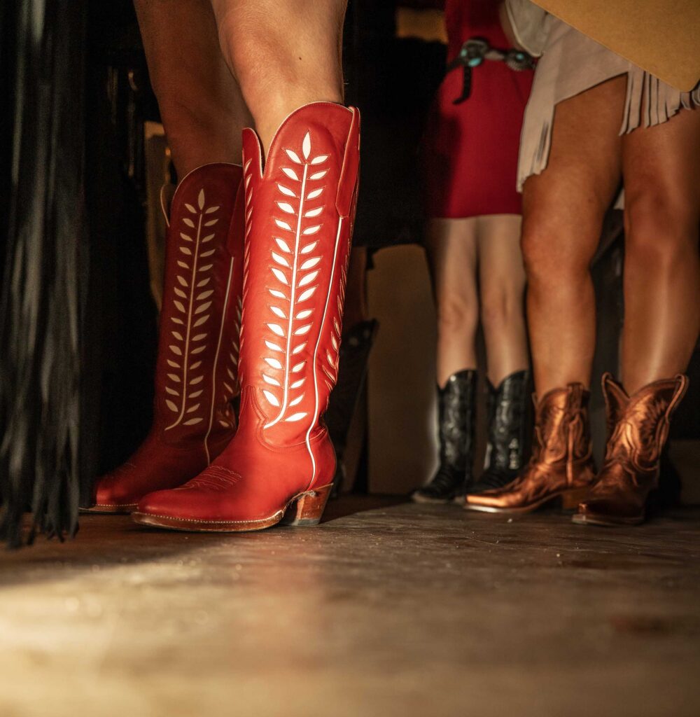Bright red cowboy boots stand among a row of partygoers.