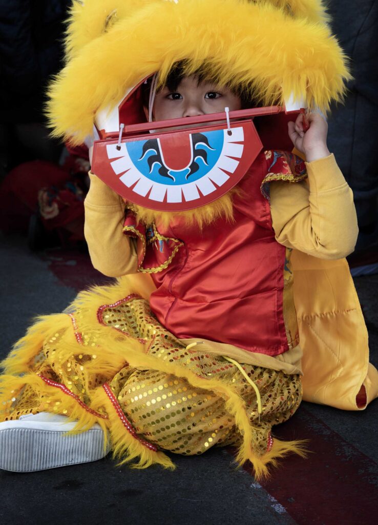 A young performer rests inside a yellow lion costume.