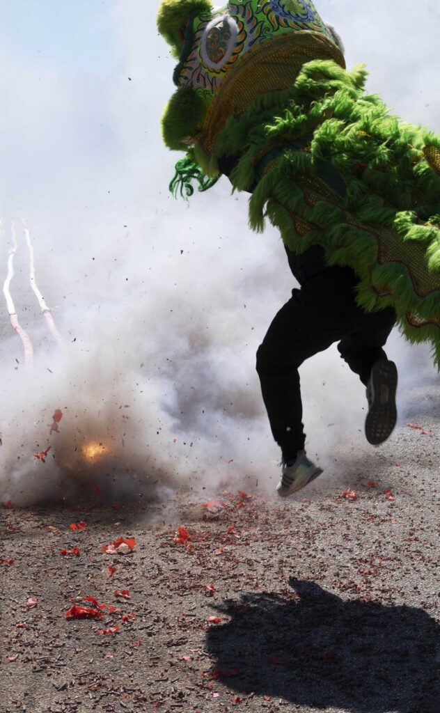 A green lion leaps through the firecracker smoke.