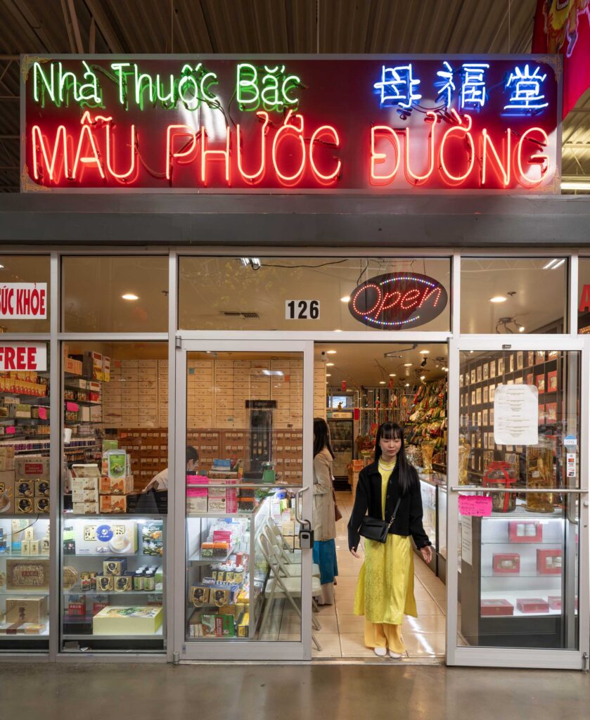 A woman in yellow steps from an herbal medicine shop at Asia Times Square.