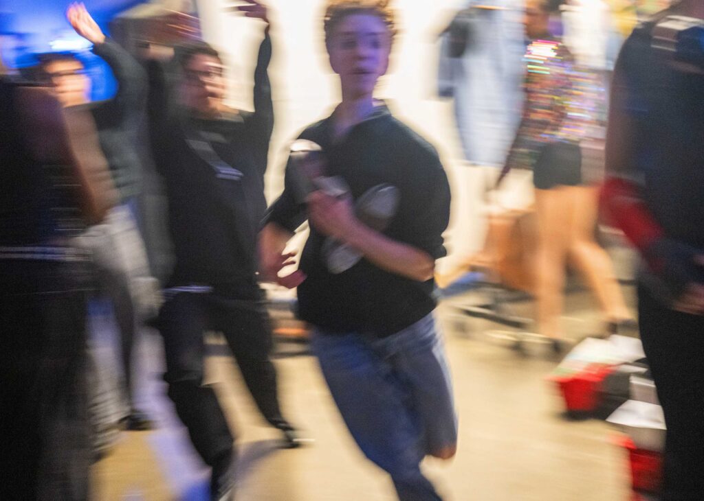 A student carrying shoes races through a busy backstage corridor.