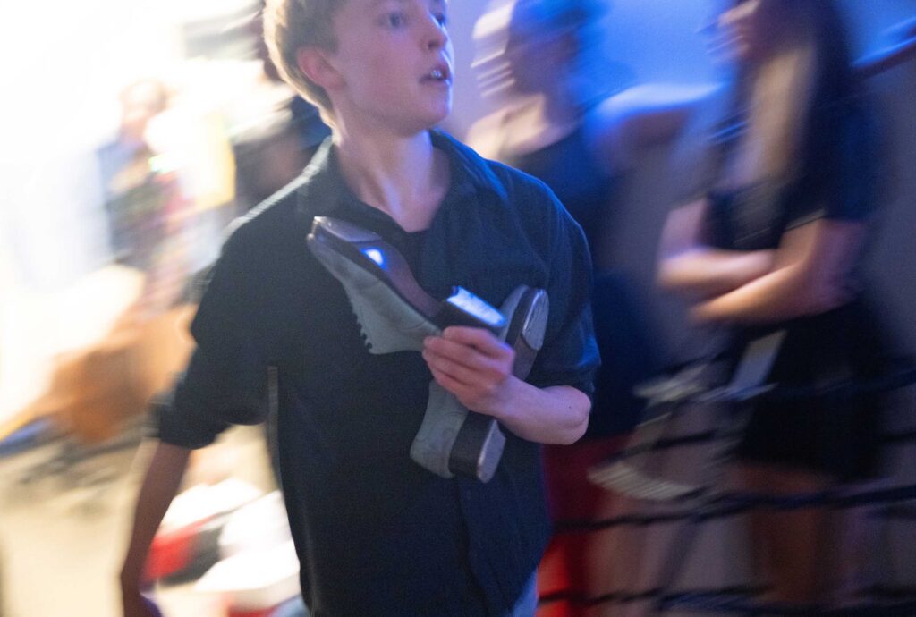 A student rushes backstage holding tap shoes after a performance.