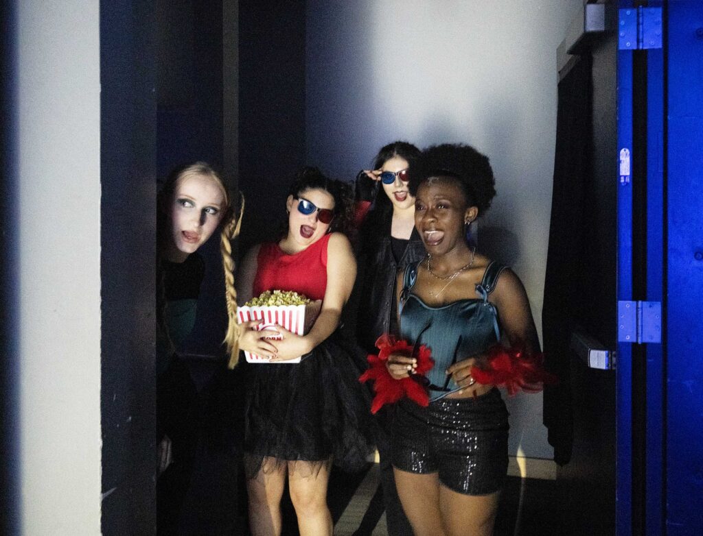 Four costumed students share a playful moment beside the stage.