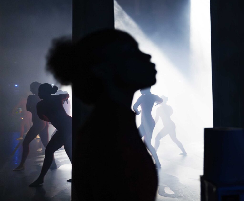Dancers perform in silhouette against bright stage light.